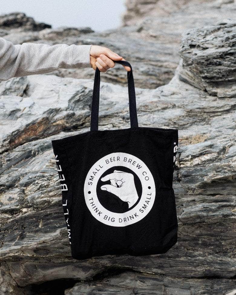 Person holding a black tote bag with Small Beer logo